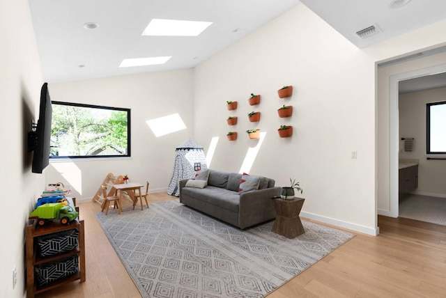 living area featuring vaulted ceiling with skylight, wood finished floors, visible vents, and baseboards