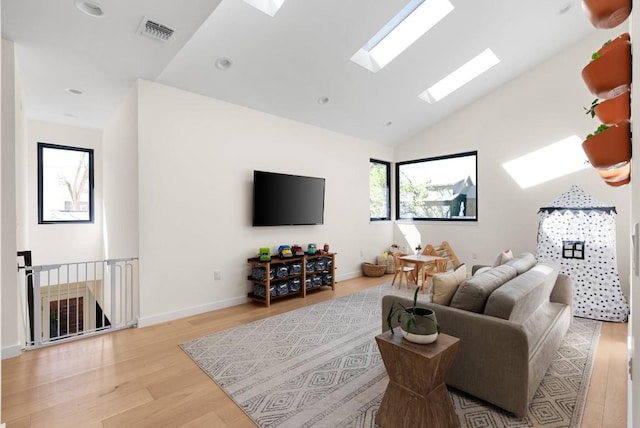 living room with a skylight, light wood finished floors, baseboards, visible vents, and high vaulted ceiling