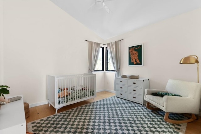 bedroom with ceiling fan, wood finished floors, baseboards, vaulted ceiling, and a crib