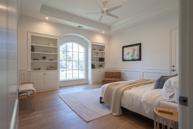 bedroom with crown molding, a raised ceiling, light wood-style flooring, and a decorative wall