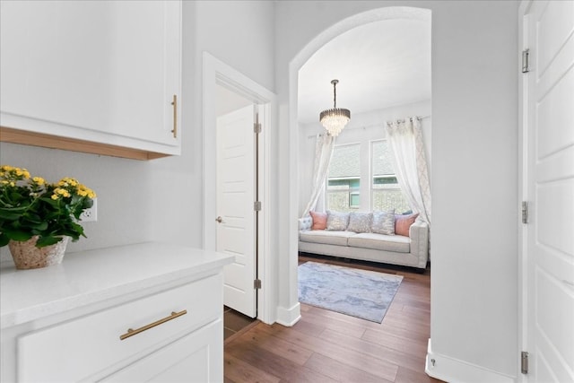 interior space featuring dark wood-type flooring, arched walkways, a chandelier, and baseboards