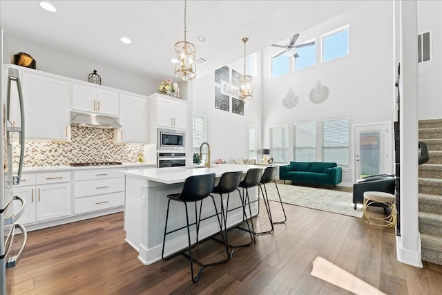 kitchen with light countertops, decorative backsplash, appliances with stainless steel finishes, dark wood-type flooring, and under cabinet range hood