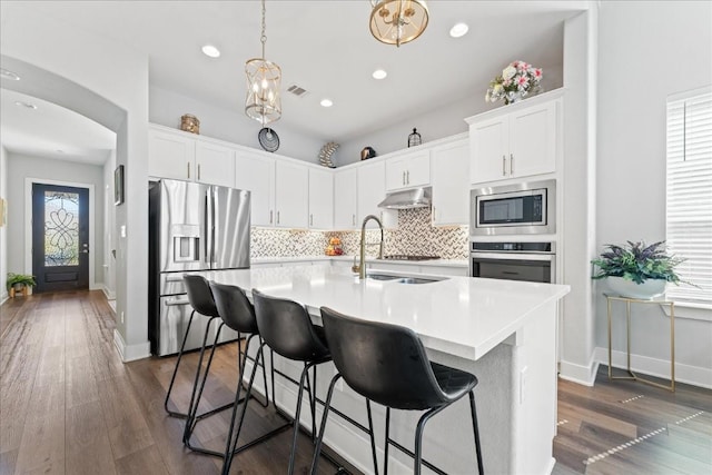 kitchen with arched walkways, under cabinet range hood, stainless steel appliances, light countertops, and tasteful backsplash