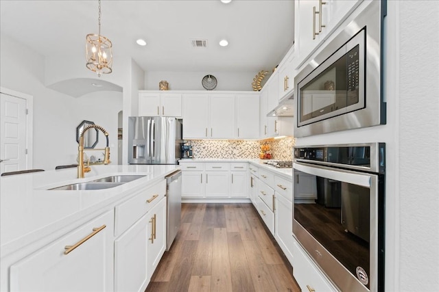 kitchen featuring under cabinet range hood, a sink, visible vents, appliances with stainless steel finishes, and decorative backsplash