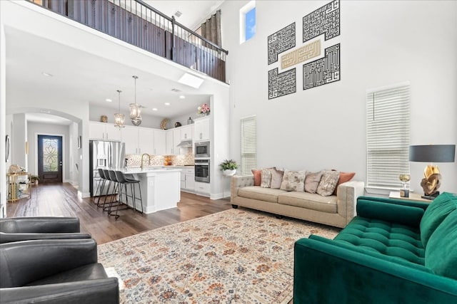 living area with arched walkways, light wood-type flooring, a towering ceiling, and baseboards