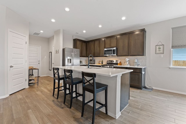 kitchen with stainless steel appliances, a sink, visible vents, dark brown cabinets, and light wood-type flooring