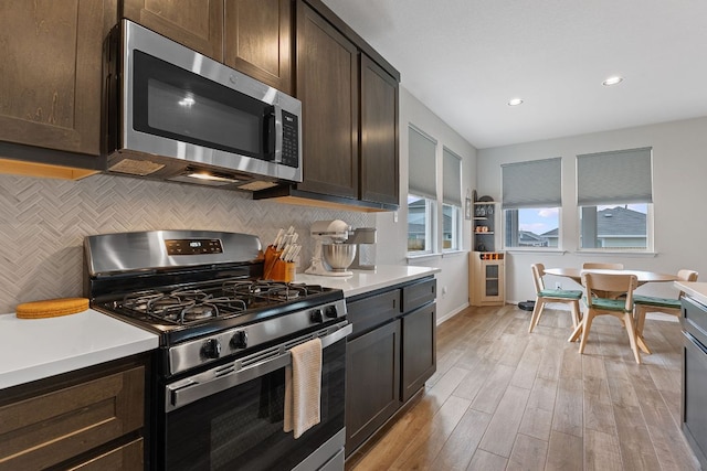 kitchen featuring dark brown cabinets, appliances with stainless steel finishes, light countertops, light wood-type flooring, and decorative backsplash