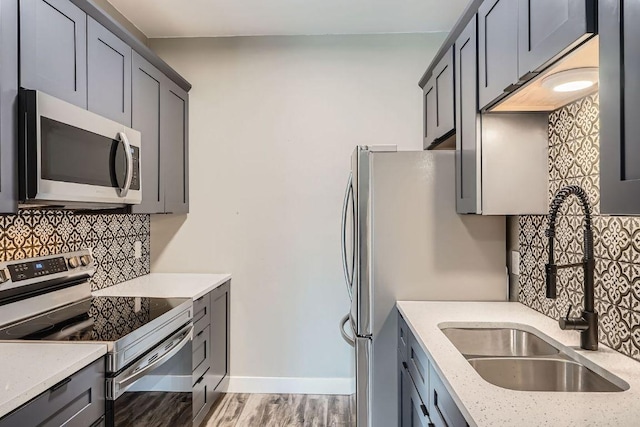 kitchen with light stone counters, stainless steel appliances, wood finished floors, a sink, and decorative backsplash