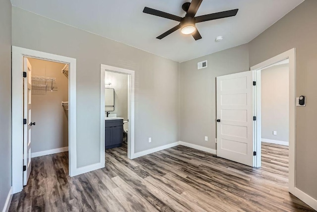 unfurnished bedroom with a walk in closet, visible vents, baseboards, and wood finished floors