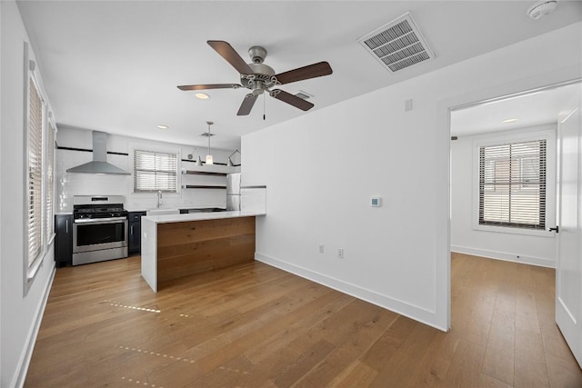 kitchen featuring a peninsula, a sink, visible vents, wall chimney range hood, and stainless steel range with gas stovetop