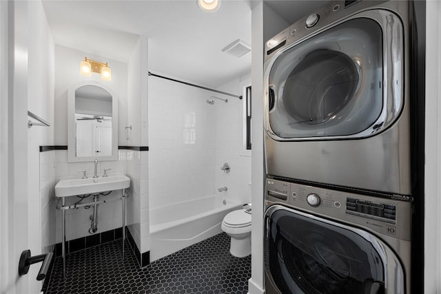 washroom featuring stacked washer and dryer, laundry area, a sink, visible vents, and tile walls