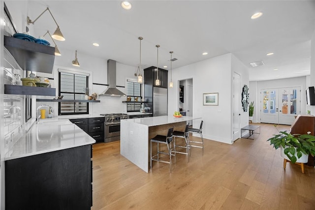 kitchen featuring wall chimney range hood, high quality appliances, open shelves, and dark cabinetry