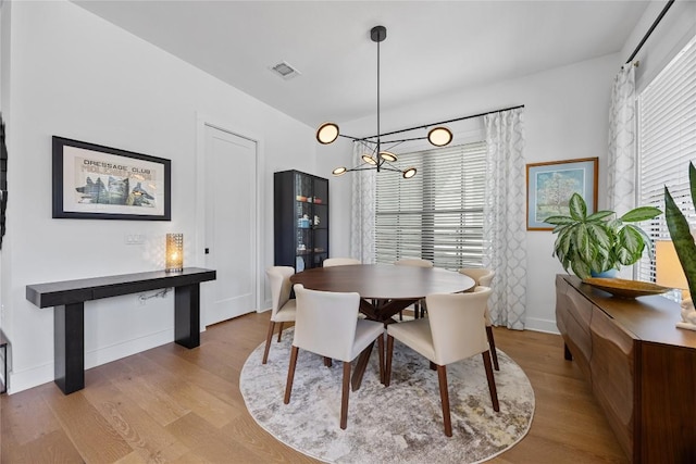 dining space featuring a chandelier, visible vents, baseboards, and wood finished floors