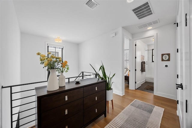 corridor featuring visible vents, baseboards, and wood finished floors