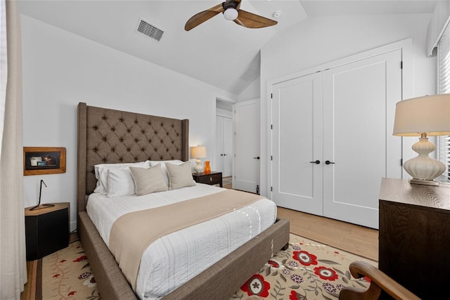 bedroom with light wood finished floors, lofted ceiling, a closet, visible vents, and ceiling fan