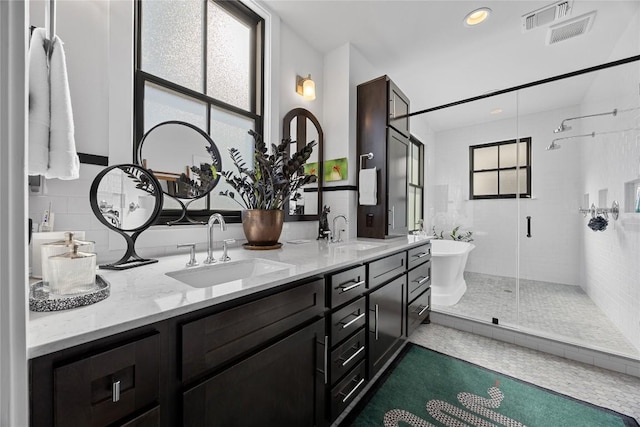 bathroom with double vanity, a shower stall, visible vents, and a sink