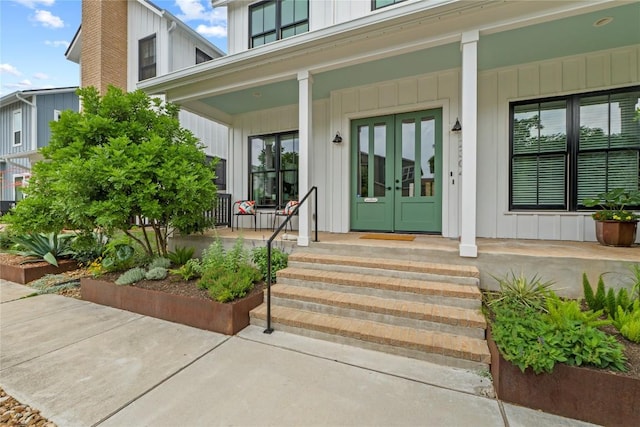 entrance to property with a porch, french doors, a chimney, and board and batten siding