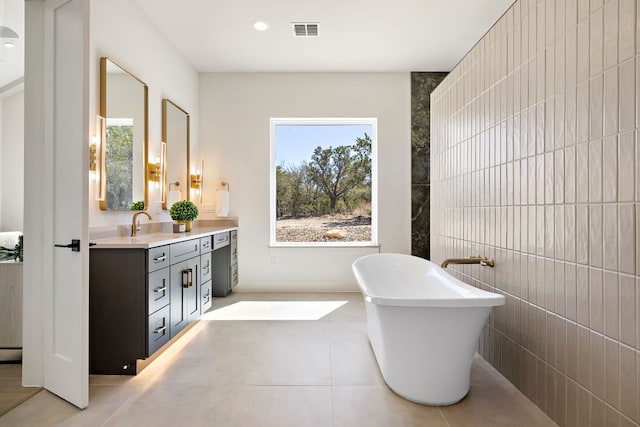 bathroom featuring tile patterned flooring, visible vents, tile walls, a freestanding bath, and double vanity