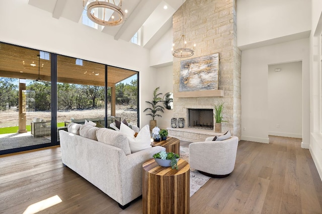 living room featuring an inviting chandelier, baseboards, wood finished floors, and a stone fireplace