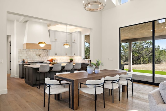 dining area featuring light wood-style floors, baseboards, a high ceiling, and an inviting chandelier