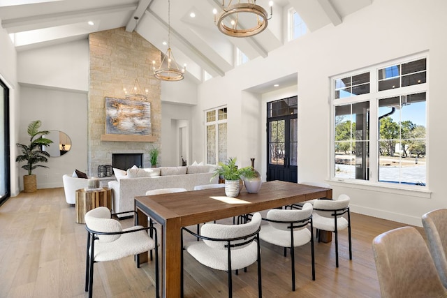 dining room featuring beam ceiling, a fireplace, a chandelier, high vaulted ceiling, and light wood-type flooring