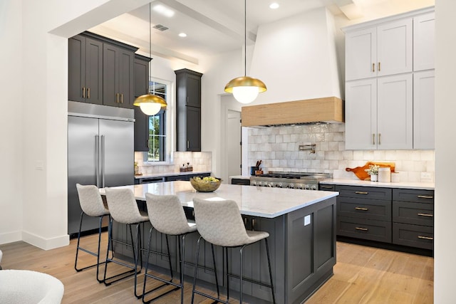 kitchen with visible vents, custom range hood, stove, light stone countertops, and built in fridge