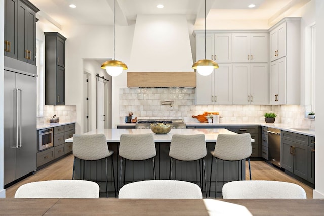 kitchen featuring stainless steel appliances, custom range hood, backsplash, a barn door, and light wood-type flooring