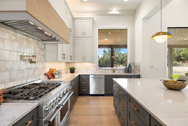 kitchen featuring custom exhaust hood, light wood-style flooring, decorative backsplash, appliances with stainless steel finishes, and a sink