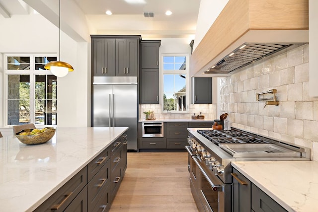 kitchen with visible vents, high end appliances, decorative backsplash, custom range hood, and light wood-style floors