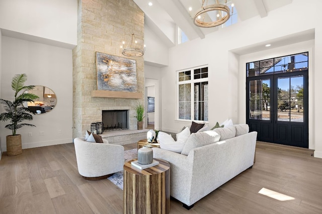 living room with a chandelier, high vaulted ceiling, a fireplace, wood finished floors, and baseboards