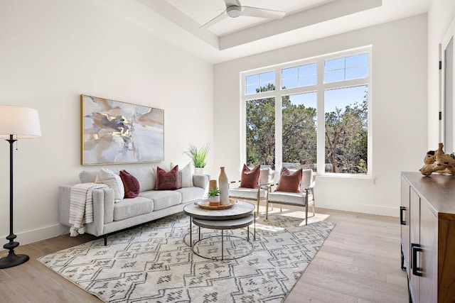 living area featuring light wood-style floors, a tray ceiling, ceiling fan, and baseboards