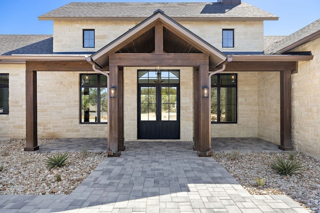 property entrance with stone siding, french doors, and a shingled roof