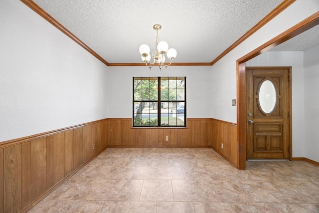 foyer entrance featuring wooden walls, wainscoting, ornamental molding, a textured ceiling, and a chandelier