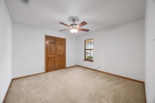 carpeted spare room with a ceiling fan, visible vents, baseboards, and a textured ceiling