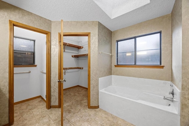 bathroom featuring a textured ceiling, a spacious closet, a garden tub, and baseboards