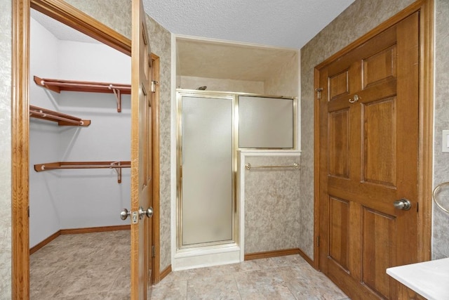 full bath featuring a walk in closet, baseboards, a shower stall, and a textured ceiling