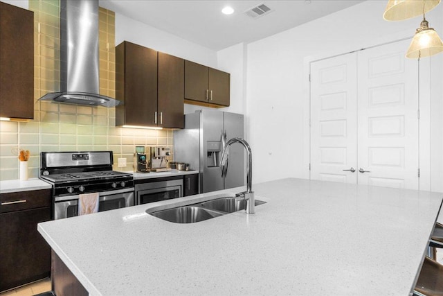 kitchen with a sink, visible vents, wall chimney range hood, appliances with stainless steel finishes, and backsplash