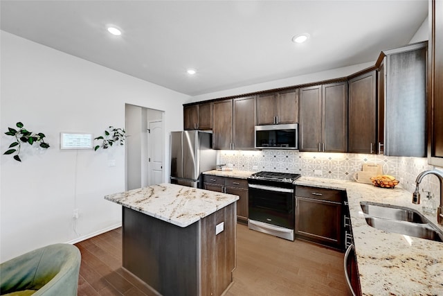 kitchen with appliances with stainless steel finishes, a center island, dark brown cabinets, light wood-style floors, and a sink