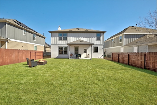 back of house featuring a fenced backyard, a fire pit, a yard, board and batten siding, and a chimney