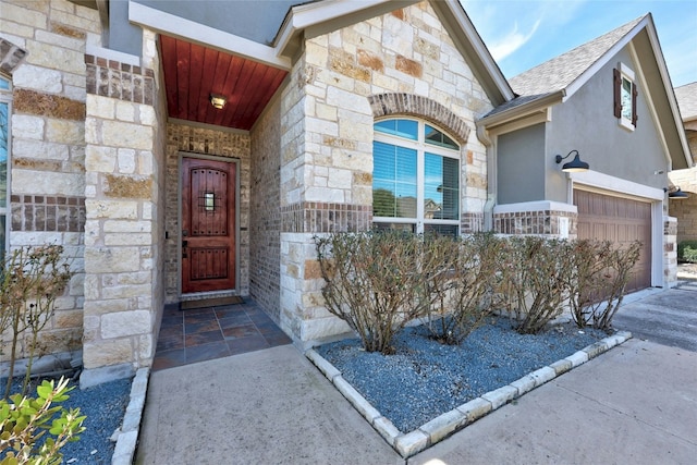 view of exterior entry with a garage, stone siding, roof with shingles, and stucco siding