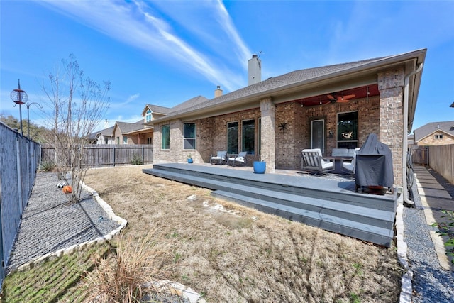 rear view of property with ceiling fan, brick siding, a chimney, and a fenced backyard