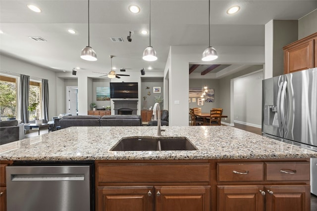 kitchen with light stone counters, a fireplace, a sink, open floor plan, and appliances with stainless steel finishes