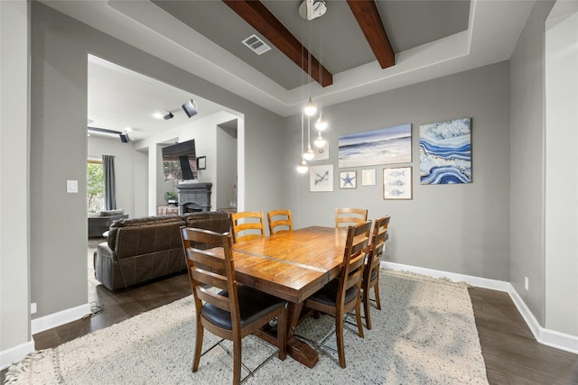 dining area with a fireplace, wood finished floors, visible vents, baseboards, and beamed ceiling