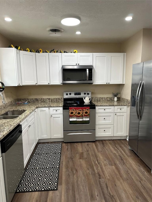 kitchen featuring light stone counters, dark wood-style floors, appliances with stainless steel finishes, white cabinets, and a sink