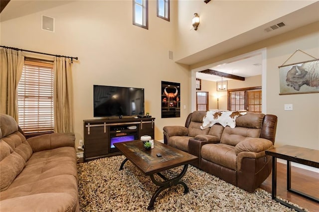 living room with visible vents, beamed ceiling, a towering ceiling, and wood finished floors