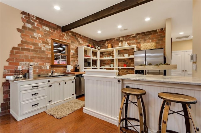 kitchen featuring brick wall, a sink, visible vents, appliances with stainless steel finishes, and beam ceiling