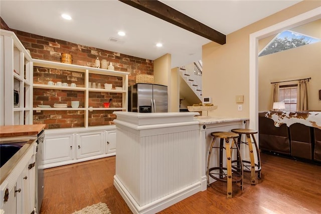 kitchen with brick wall, wood finished floors, beam ceiling, and stainless steel fridge with ice dispenser