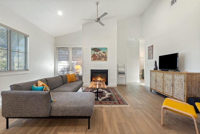 living area with ceiling fan, high vaulted ceiling, a fireplace, wood finished floors, and visible vents