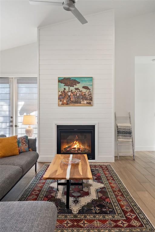 living room with a large fireplace, baseboards, a ceiling fan, lofted ceiling, and wood finished floors