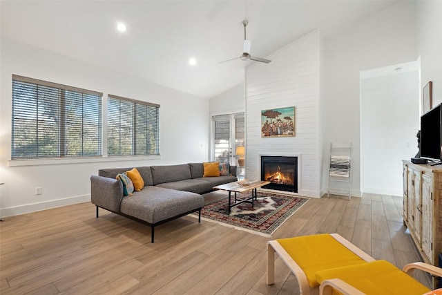 living room with high vaulted ceiling, a large fireplace, a ceiling fan, baseboards, and light wood-style floors